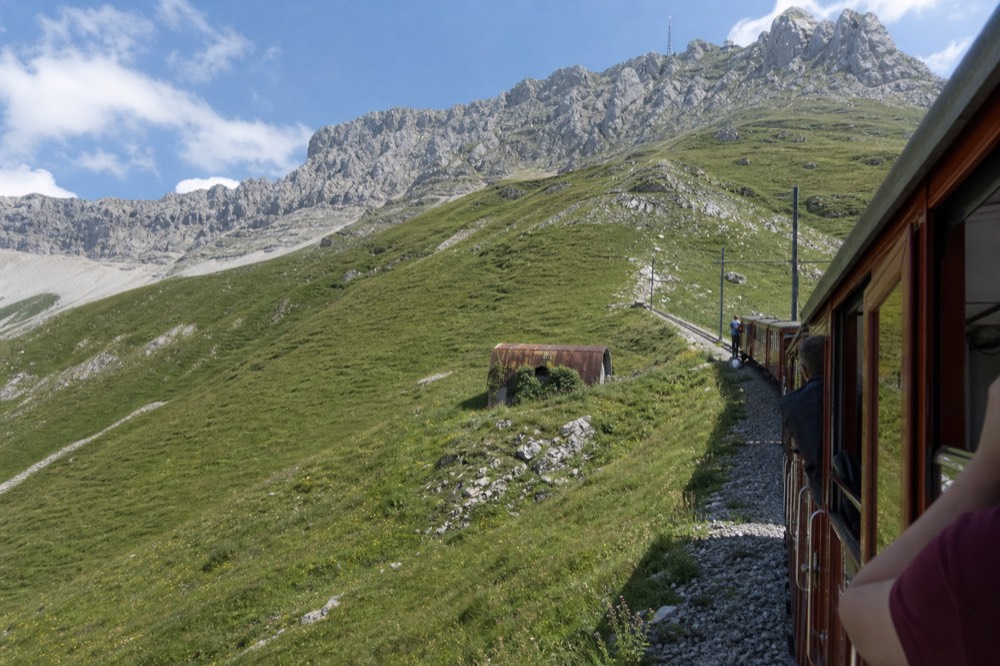 Cogwheel railway climbing a steep green mountainside toward a rocky summit, no text, no logos, no people