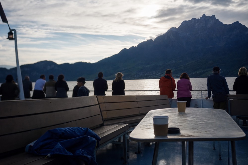 Passengers on a boat deck approaching a steep mountain slope across blue water, no text, no logos, no people