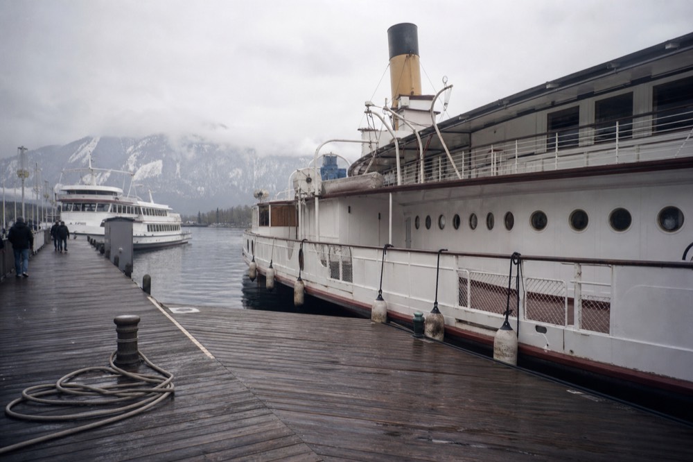 Historic paddle steamer and white boats moored at a lakeside pier below mountains, no text, no logos, no people