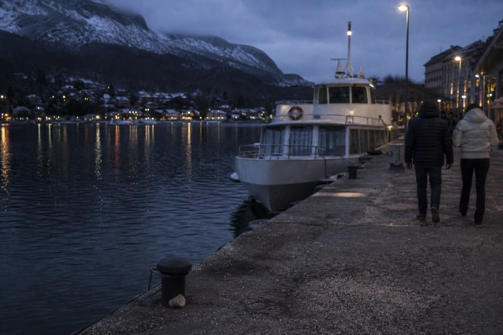 A lakeside quay with a moored passenger boat and mountains across the water, no text, no logos, no people.