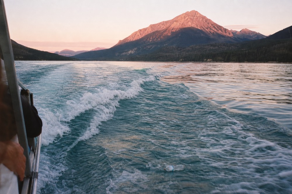 A boat wake trailing across blue water toward a mountain summit, no text, no logos, no people.