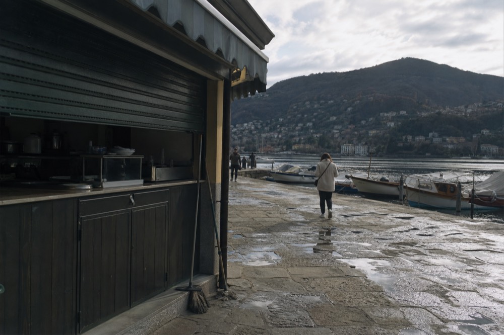 A ticket kiosk and moored boats along a lakefront quay, no text, no logos, no people.