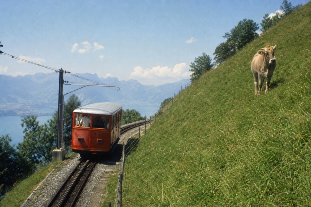 Red cogwheel railway car ascending steep green slopes toward Pilatus summit, no text, no logos, no people