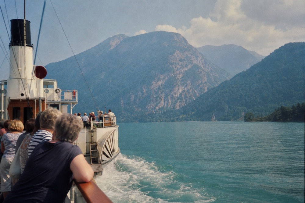 Historic paddle steamer crossing turquoise water beneath mountain slopes, no text, no logos, no people